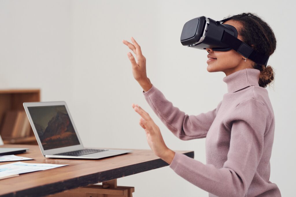 Woman using VR headset at desk with laptop, exploring virtual reality.