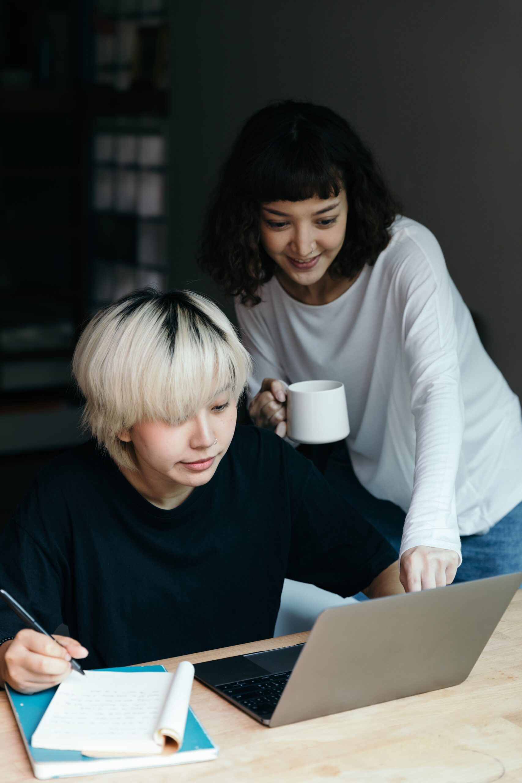 Two people collaborating and studying together at a table with a laptop and notebook.